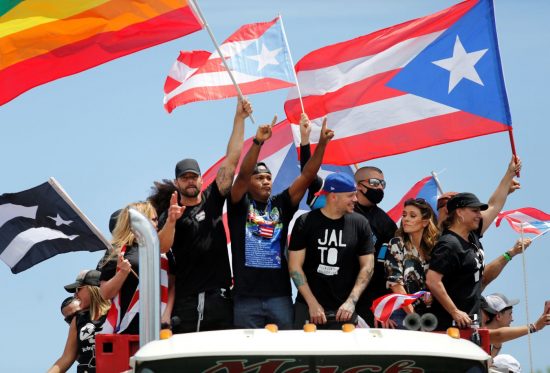 Ricky Martin waves the LGBTQ Rainbow Flag as others wave the Puerto Rican flag at protests